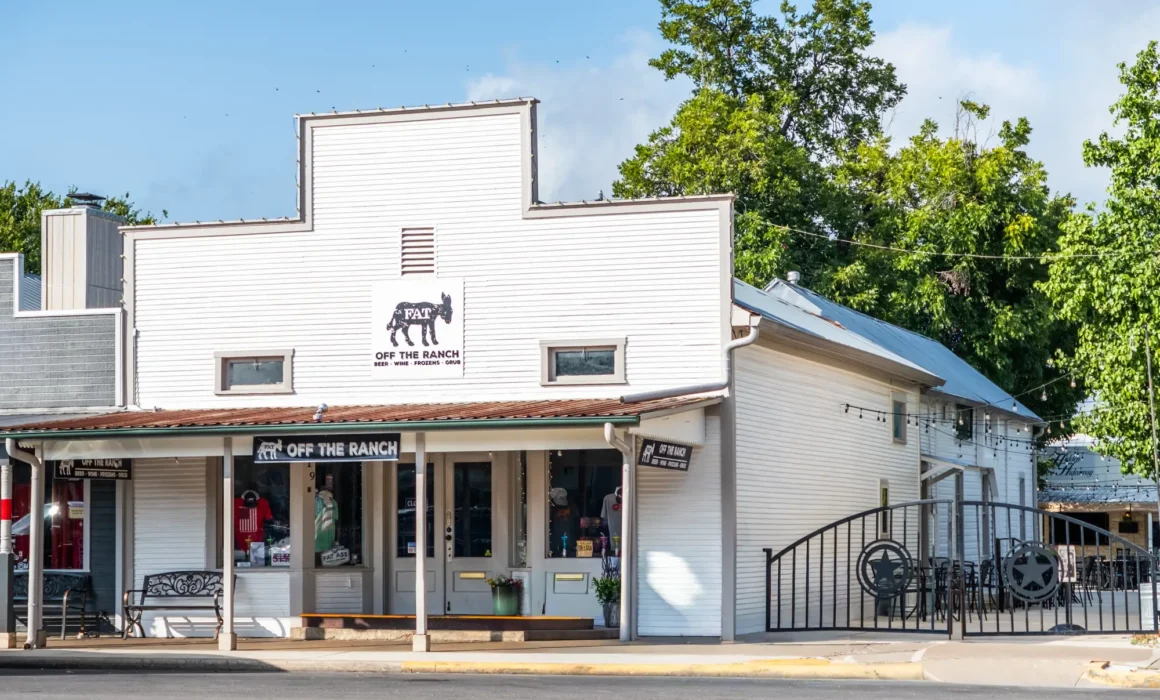 Front view of the white false-front Fat Ass Ranch building at 319 with a covered porch and rocking chairs