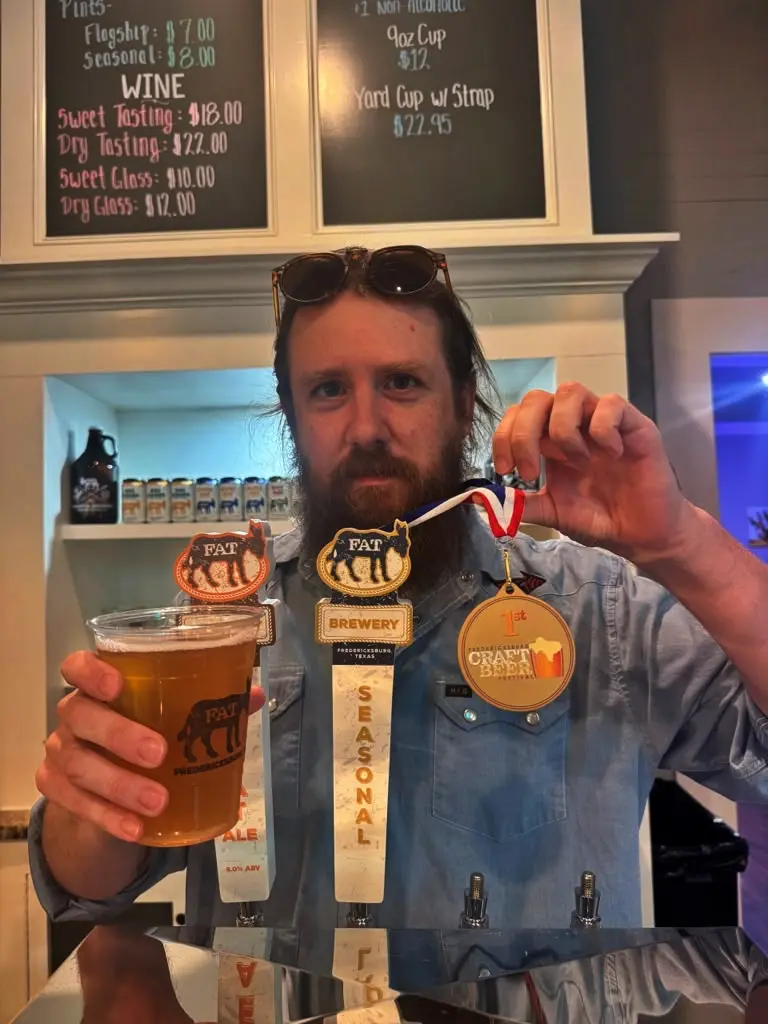 Travis holding a pint of beer and his gold medal from the Fredericksburg Craft Beer Festival at the taproom bar